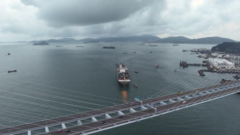 cars driving over a suspension bridge while a large container ship approach the port on a cloudy day