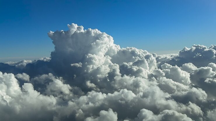 An immersive pilot’s eye perspecvtive taken from the cockpit of a jet airplane flying above a cottony storm clouds under a deep blue sky, in a right turn to avoid bad weather. Ultra-reaslistic 4K