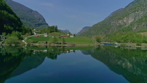 Aerial-flight-over-calm-fjord-water-reaching-green-island-between-mountains-in-Norway