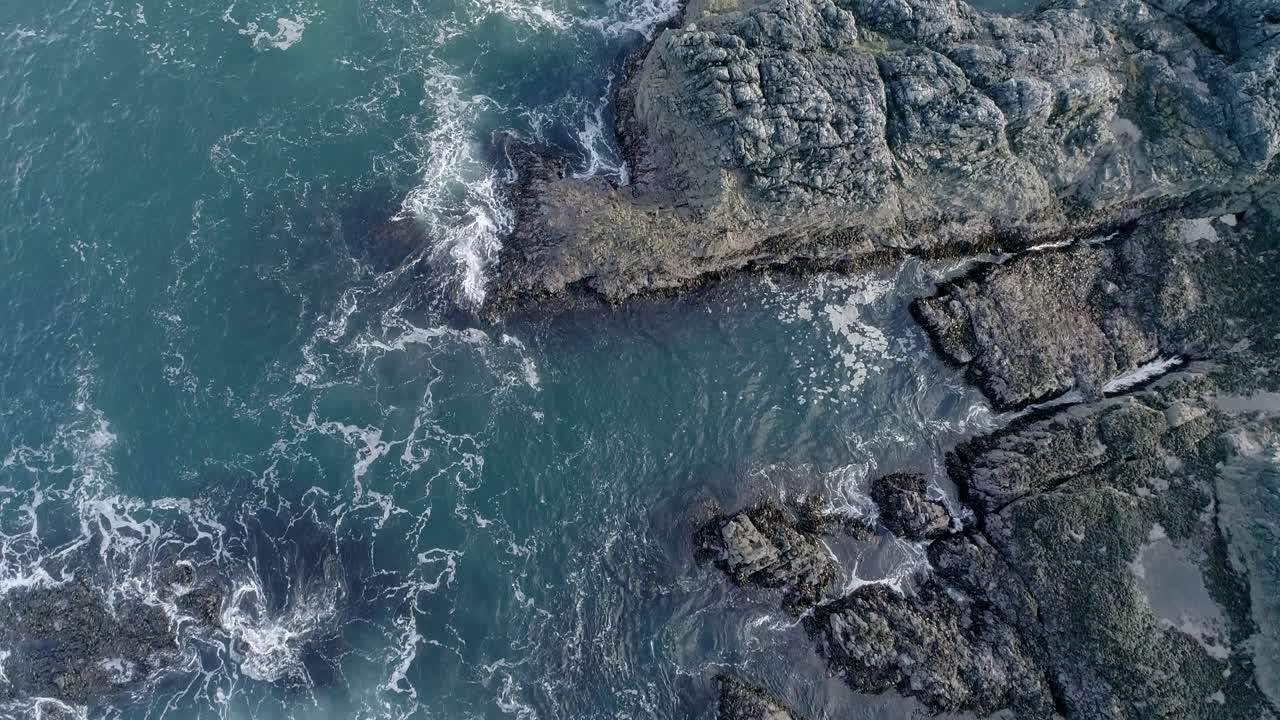 Rough sea waters brushing over low lying rocky coastline surrounded by rockpools and lots of seaweed