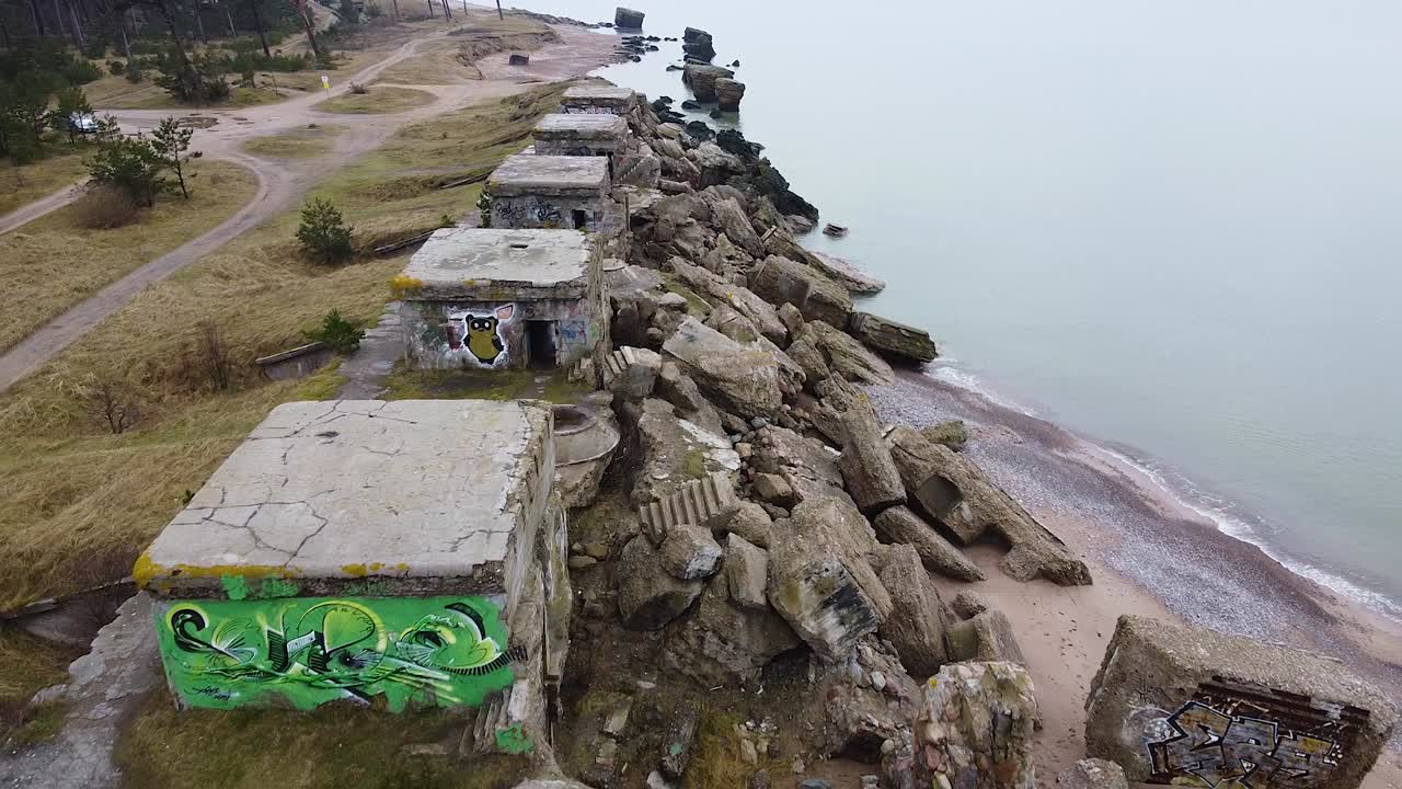 Aerial view of abandoned seaside fortification building at Karosta Northern Forts on the beach of Baltic sea in Liepaja in overcast spring day, wide establishing drone shot moving backwards
