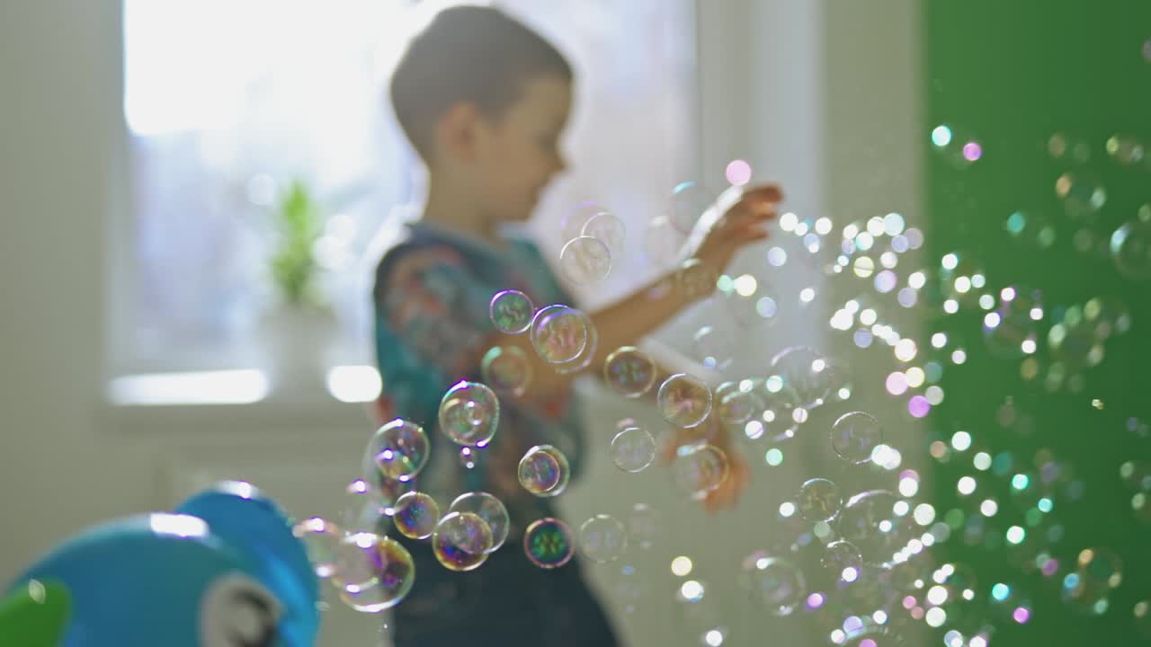 Many aqua bubbles flying in the room on blurred background with a little boy. Cute child having fun with soap bubbles indoors.