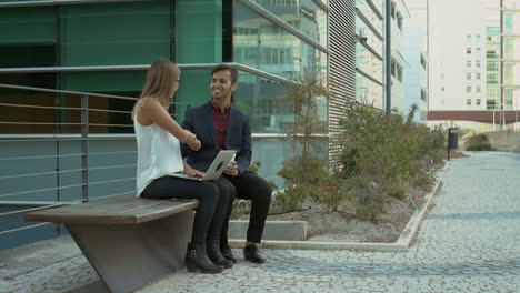 smiling business people using laptop and shaking hands