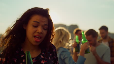 Afro-woman-celebrating-with-beer-on-rooftop.-African-girl-dancing-at-party.