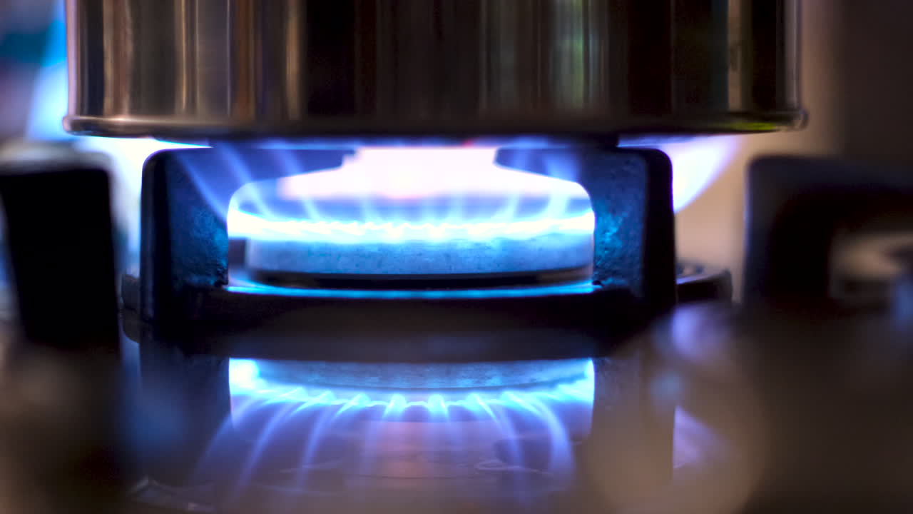 Gas burner of stove with blue flame heating up and boiling water of kettle