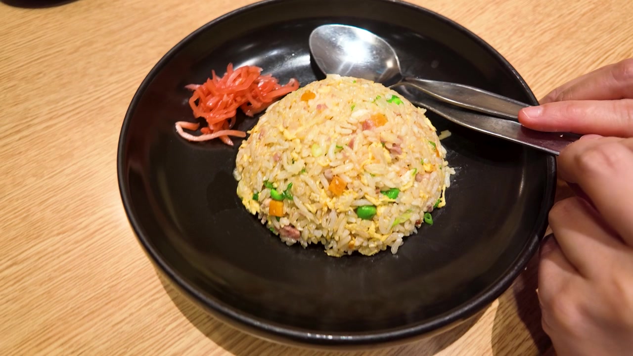 Tangkapan sudut tinggi tangan memegang peralatan makan di atas nasi goreng di piring hitam