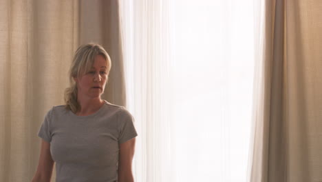 woman in pajamas opening curtains