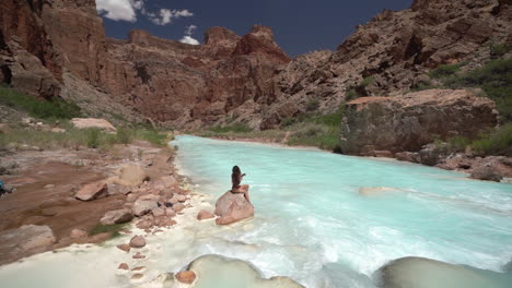 Young-Woman-in-Bikini-Sitting-on-Rocky-by-Turquoise-River-Water,-Grand-Canyon-National-Park,-Arizona-USA