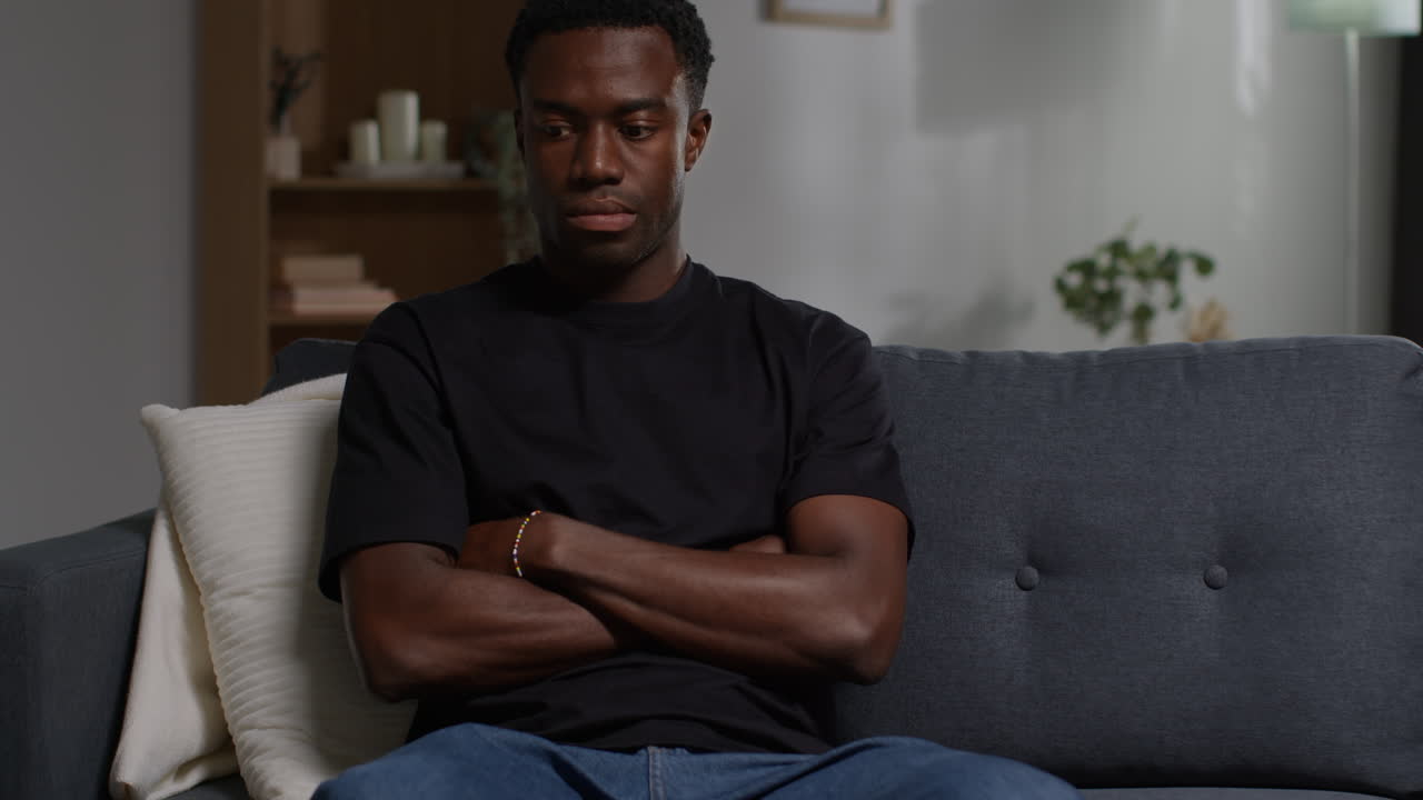 Unhappy And Depressed Young Man Sitting On Sofa At Home Looking Anxious And Worried Resting Head On Hand