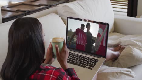 Composite-of-woman-sitting-at-home-holding-coffee-watching-hockey-match-on-laptop