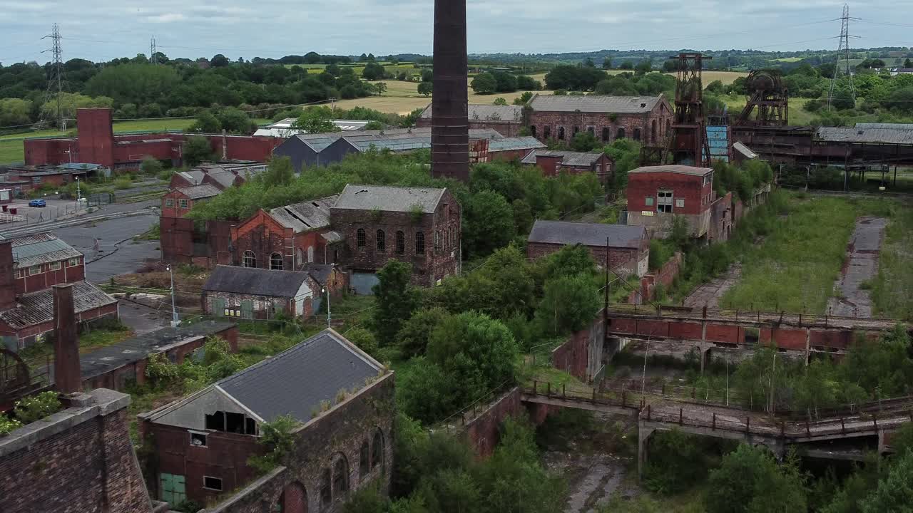 Veduta aerea in avanzamento di vecchi edifici di un museo industriale, ex miniera di carbone abbandonata e ricoperta di vegetazione.