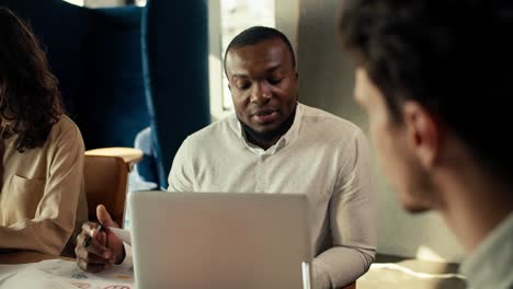 A-black-skinned-person-communicates-with-a-man-in-a-shirt-at-a-table-in-the-office.-Business-communication-of-workers-in-the-office-in-shirts