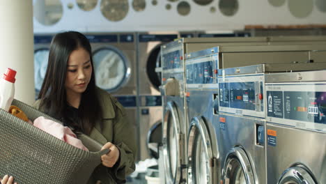 asian beautiful young woman carrying basket with diry clothes and abstergent while coming to laundry service. pretty girl coming to wash clothing.