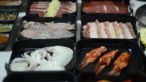 carnes y mariscos aromatizados junto con un montón de salsas en recipientes negros