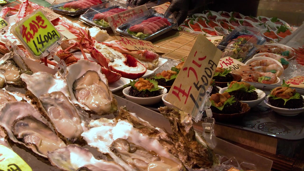 Close-up shot of raw oysters, crab legs, and sashimi on ice at a market