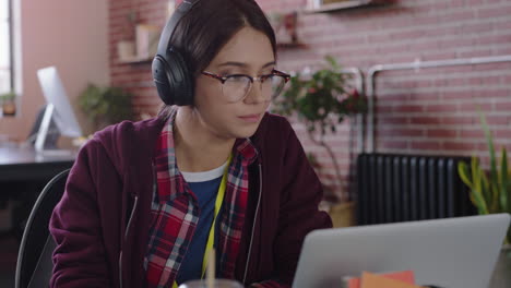 young-caucasian-woman-student-using-laptop-computer-browsing-online-working-on-project-drinking-juice-listening-to-music-in-modern-trendy-office