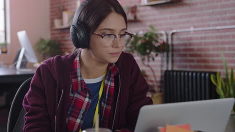 joven estudiante caucásica usando una computadora portátil navegando en línea trabajando en un proyecto bebiendo jugo escuchando música en una oficina moderna y de moda