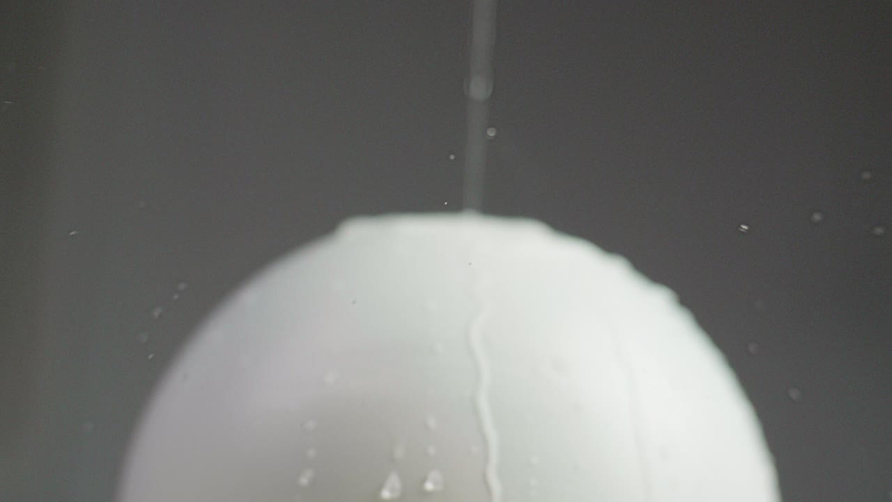 Close up of a white plain sphere wet with water pured on running along the sphere. A dark gray background. Shot in Slow Motion in 4K.