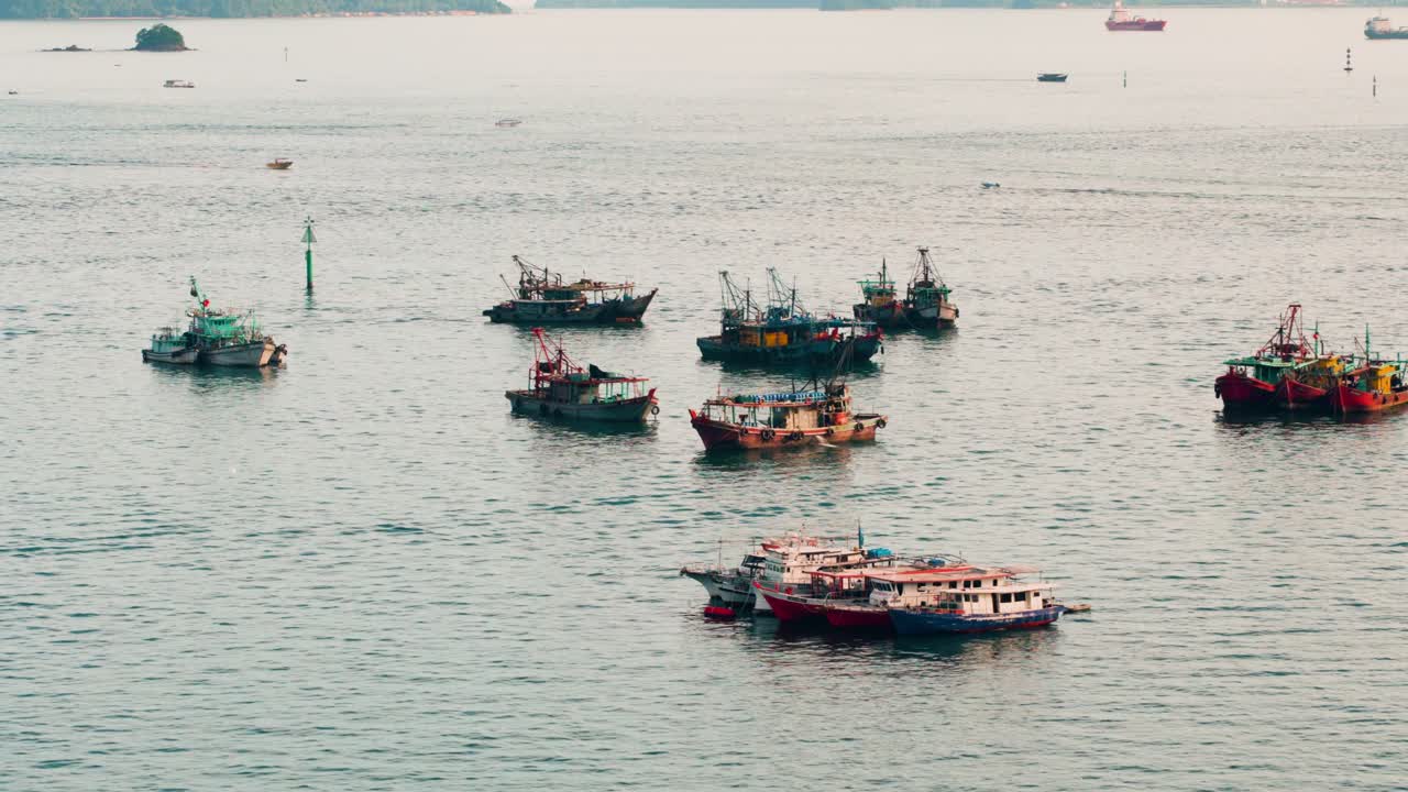 High angle aerial drone shot of a group of traditional fishing trawlers floating on the calm sea in the Kota Kinabalu port, Sabah, Malaysia during sunset
