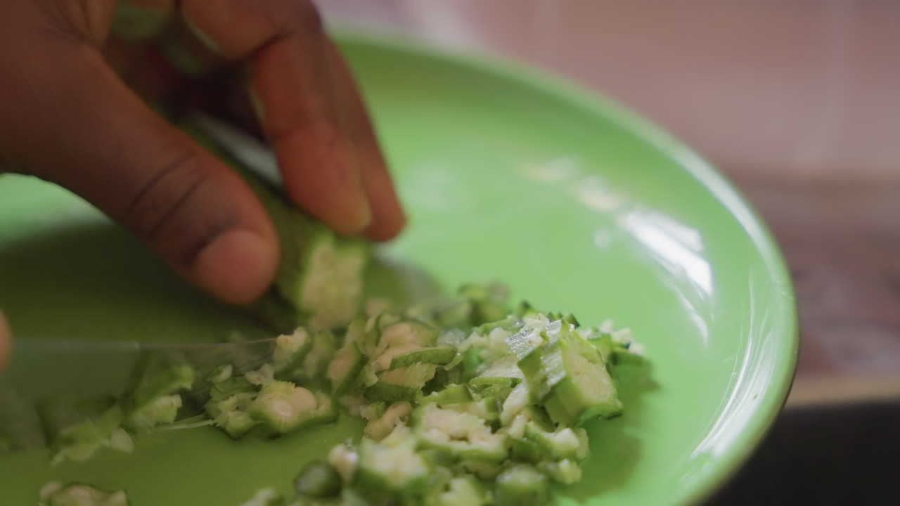 Nærbillede af mørke hænder, der hakker agurk på en grøn tallerken, forberedelse i hjemmekøkken, afslappet rytme, fint hakket til frisk salat, naturligt lys, blide ASMR-knivlyde, fokus på ingredienser, enkelt sundt måltid.