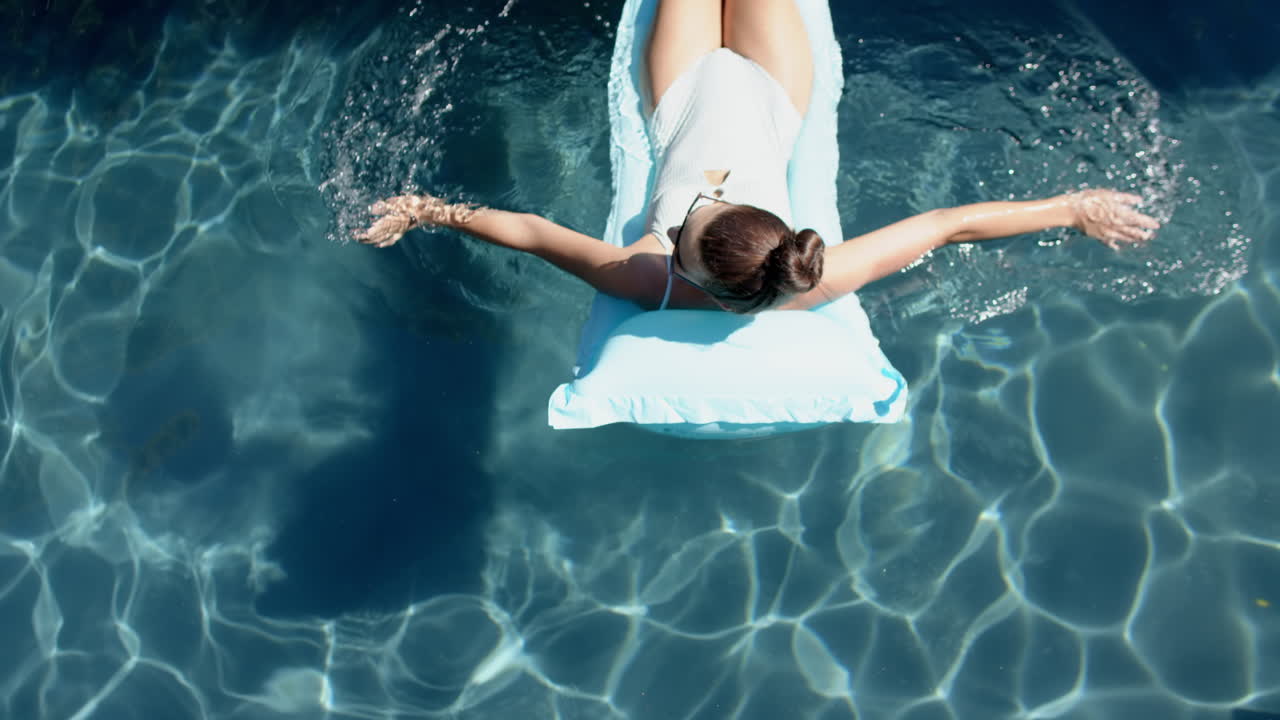 Teenage Caucasian girl relaxes on a float in a sunlit pool, her hair tied back