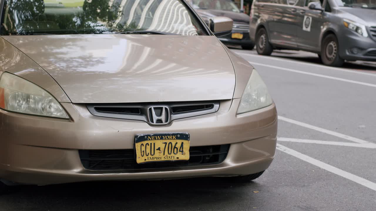 A gold Honda parked on a street in New York City with cars in the background