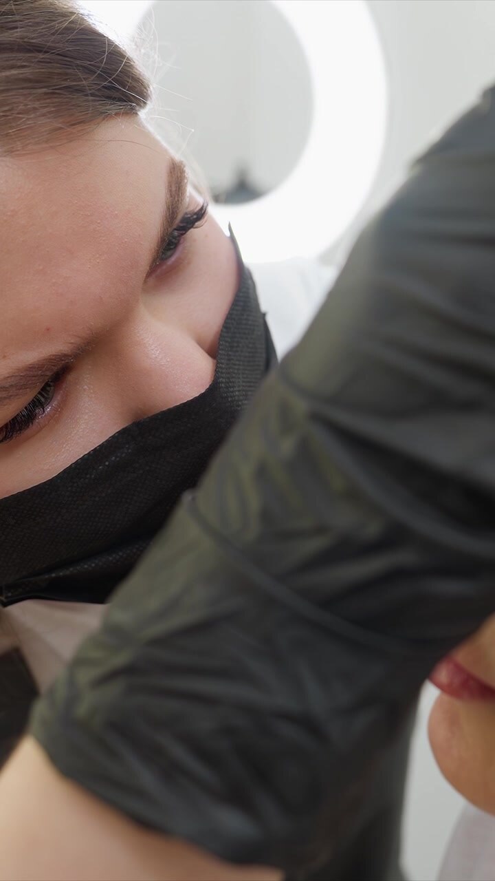 Woman receives eyebrow shaping treatment. focus is on close up interaction between her face and gloved hands performing precise beauty care gloves closeup