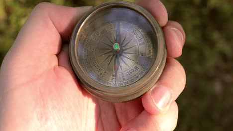 traveler hand holds a old directional compass in summer forest. person use compass to find location. travel concept close-up.