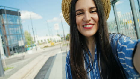 close-up view of caucasian young happy woman traveller in hat talking, waving hands and smiling at the camera outdoors in summer