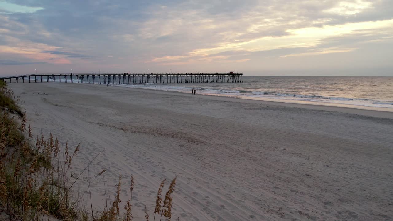 Ripresa aerea di avena marina all'alba con un molo sullo sfondo a Kure Beach, Carolina del Nord.