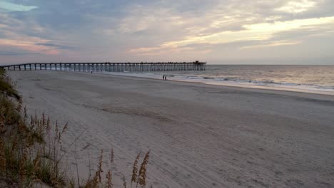 aerial over sea oats at sunrise with pier in background at kure beach nc, north carolina