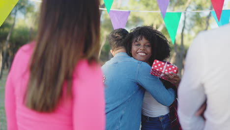 happy friends hugging and celebrating with a gift at an outdoor party