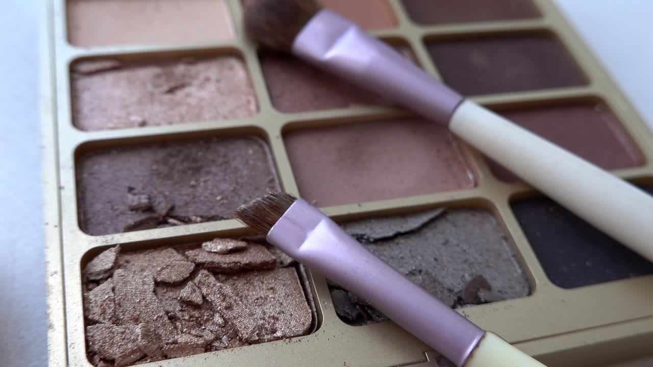 Close up of two purple make-up brushes on an eyeshadow palette