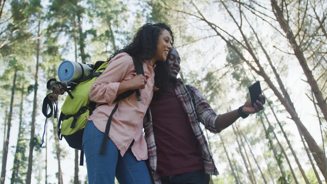 pareja divertida sonriendo usando un teléfono inteligente y caminando en el campo