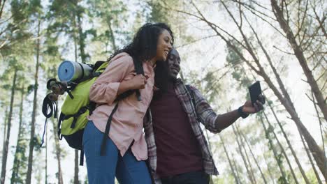 Smiling-diverse-couple-using-smartphone-and-hiking-in-countryside