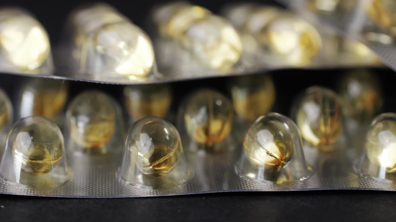 Wrapped omega fish oil gel capsules on black background close-up . Omega vitamins pills 3 6 9. To be healthy and take care of your health. Pharmaceutical industry. Business of biological supplements and vitamin. Pharmacy store delivery