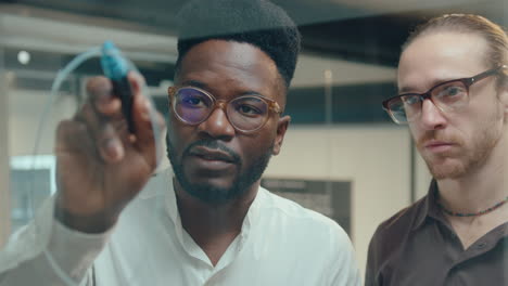 Black Man Drawing Chart on Glass Office Wall and Talking with Colleague