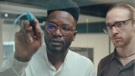 black man drawing chart on glass office wall and talking with colleague