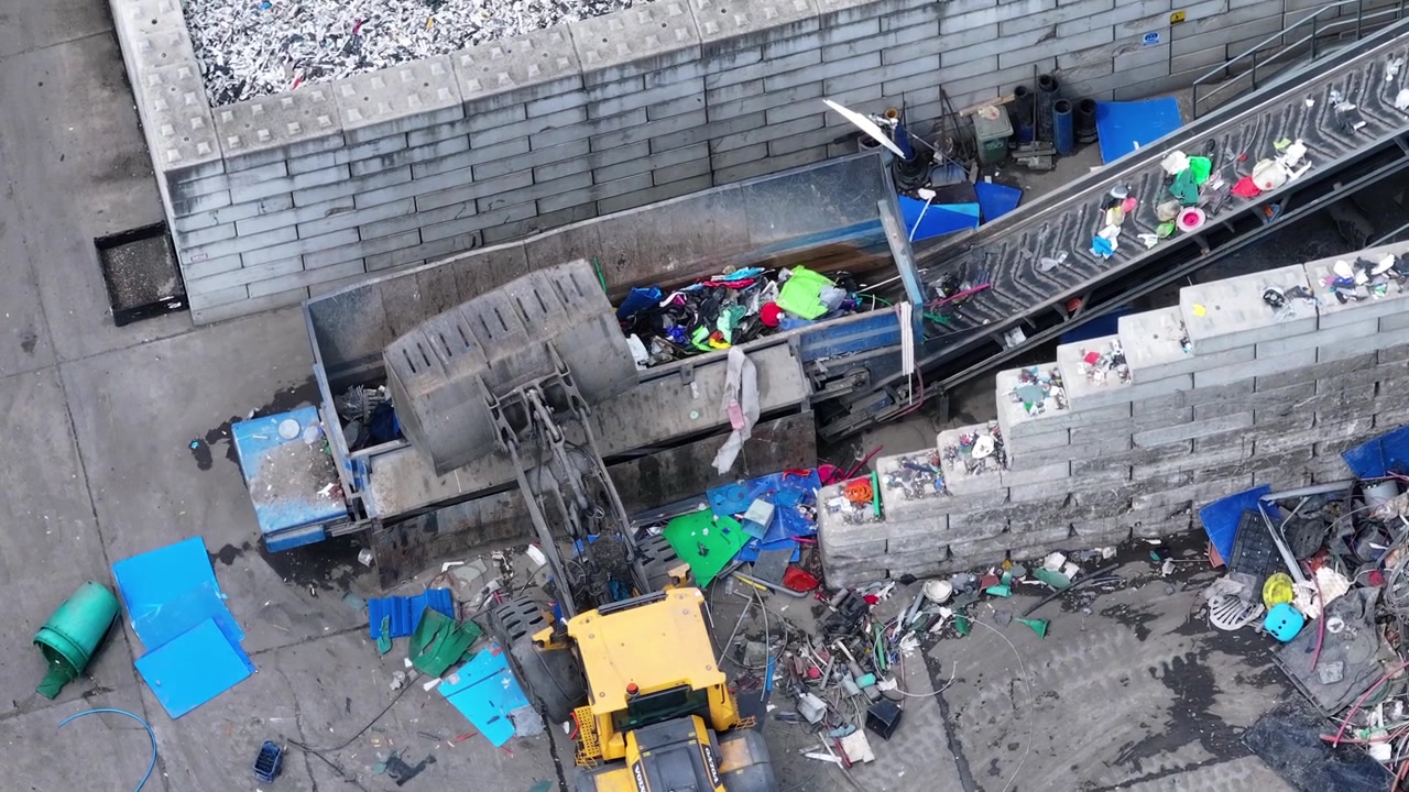 Plastic waste enters the facility on a conveyor belt. Workers sort recyclable materials from non-recyclable. Machinery processes plastic for recovery.