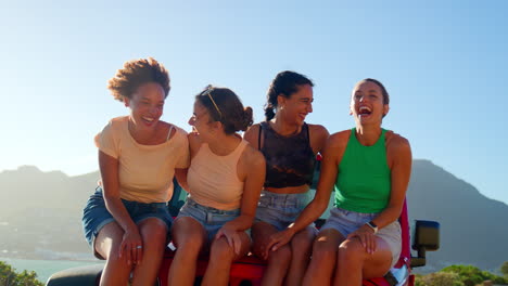 retrato de amigas riendo sentadas en el capó de un coche abierto en un viaje por carretera