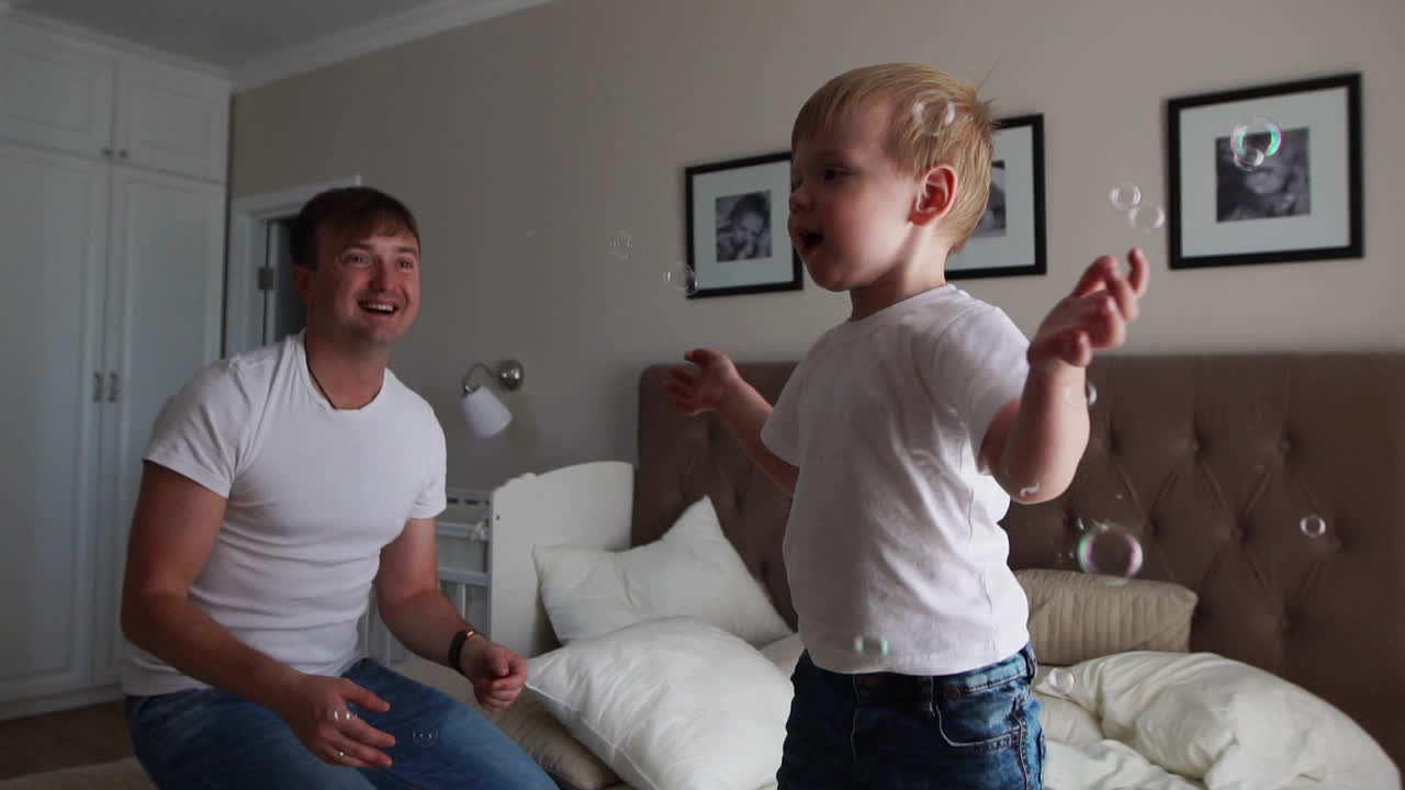 Dad plays with his son in the bedroom catching soap bubbles smiling and laughing