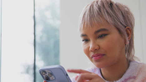 Close-Up-Of-Young-Woman-At-Home-Scrolling-Through-Social-Media-On-Mobile-Phone