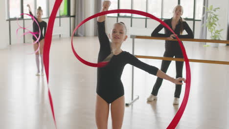 two young girls practising rhythmic gymnastics with a ribbon while female teacher watching them 1