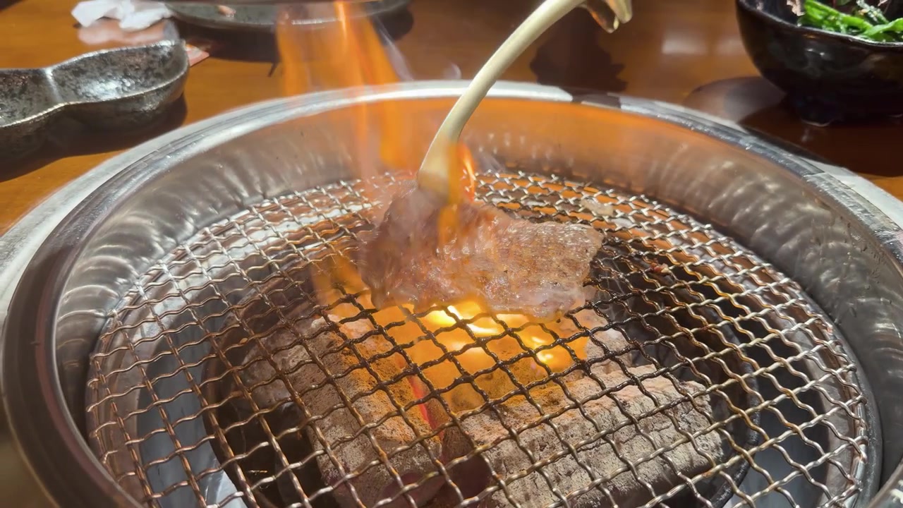 鮮やかなオレンジ色の炎が上がる炭火グリルで焼かれる上質な牛肉のクローズアップショット
