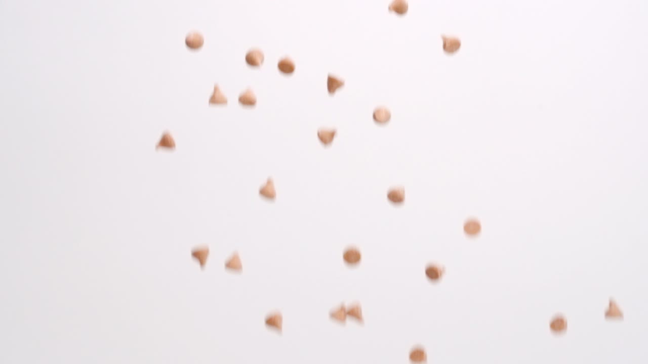 Scaglie di caramello butterscotch che piovono su uno sfondo bianco in slow motion.