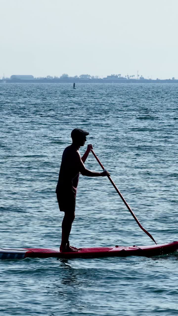 Paddle surfer paddling on calm water. Vertical