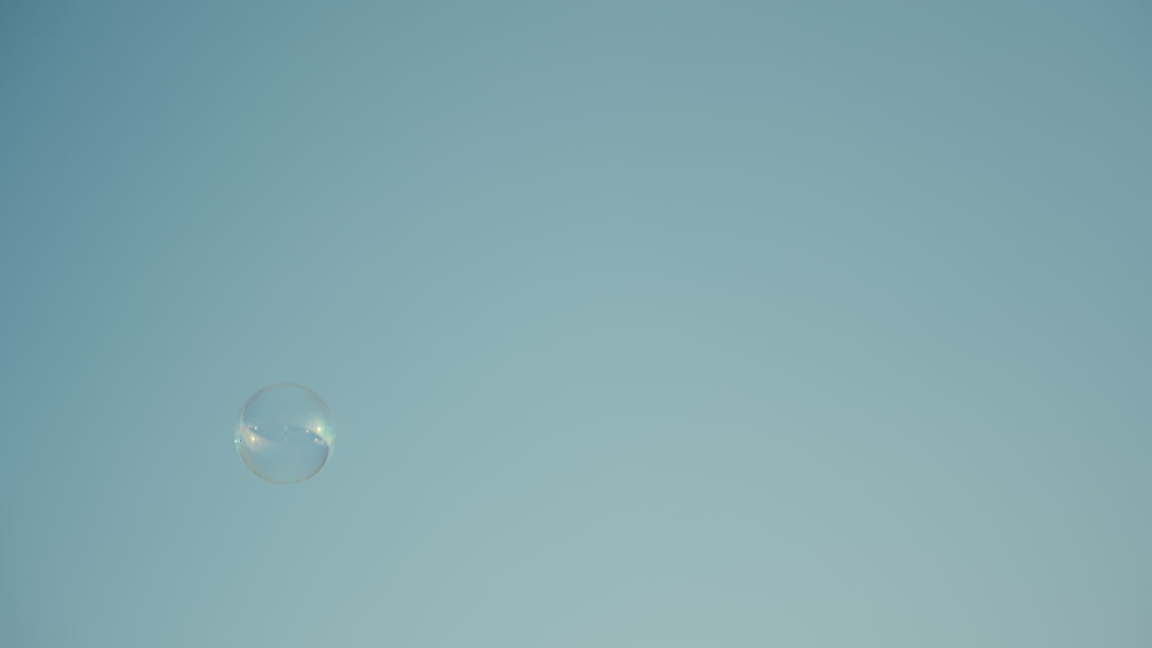 Close up of single translucent bubble drifting gently against bright blue sky, sunlight reflecting subtle rainbow hues on surface, minimalistic dreamy