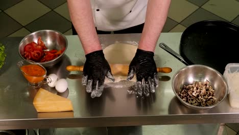 close-up of a chef rolling out pizza dough with a rolling pin in the kitchen.