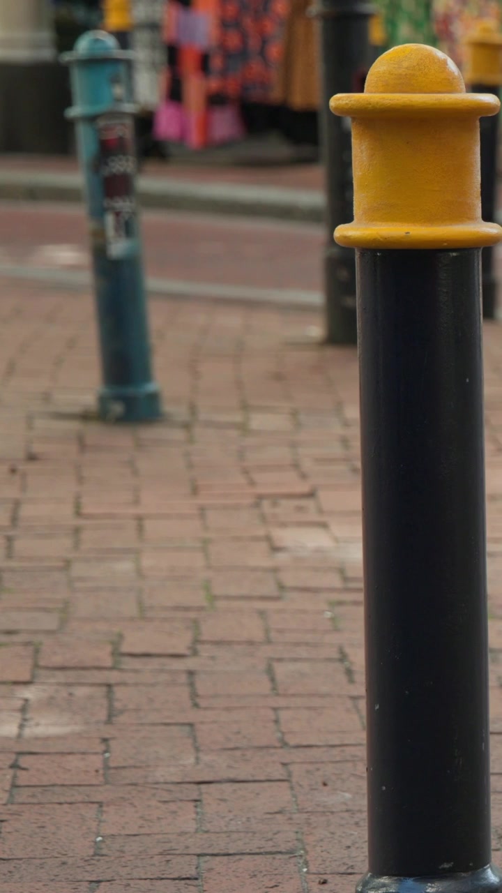 Vertical video: Clip opening on mint capri walking with bag on brick path past bollard, copy space