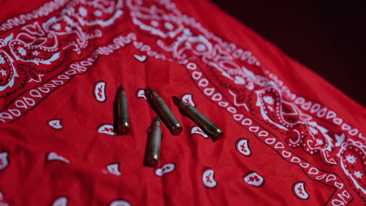 Primo piano cinematografico di cartucce di proiettili posizionate su una bandana rossa: concetto per conflitti tra gang, violenza urbana, simbolismo del crimine e indagini delle forze dell'ordine